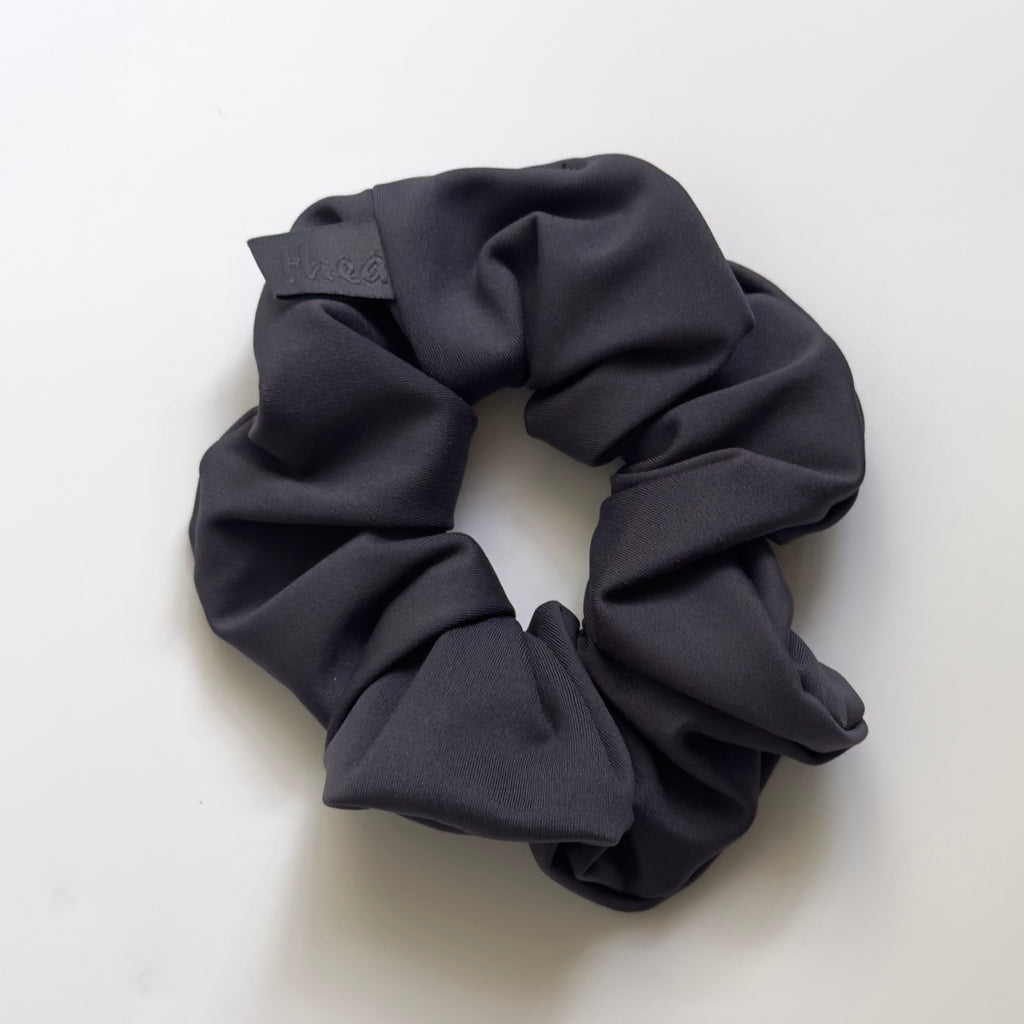 A dark navy fabric scrunchie with a small navy fabric tag on the side, photographed on a clean white background.