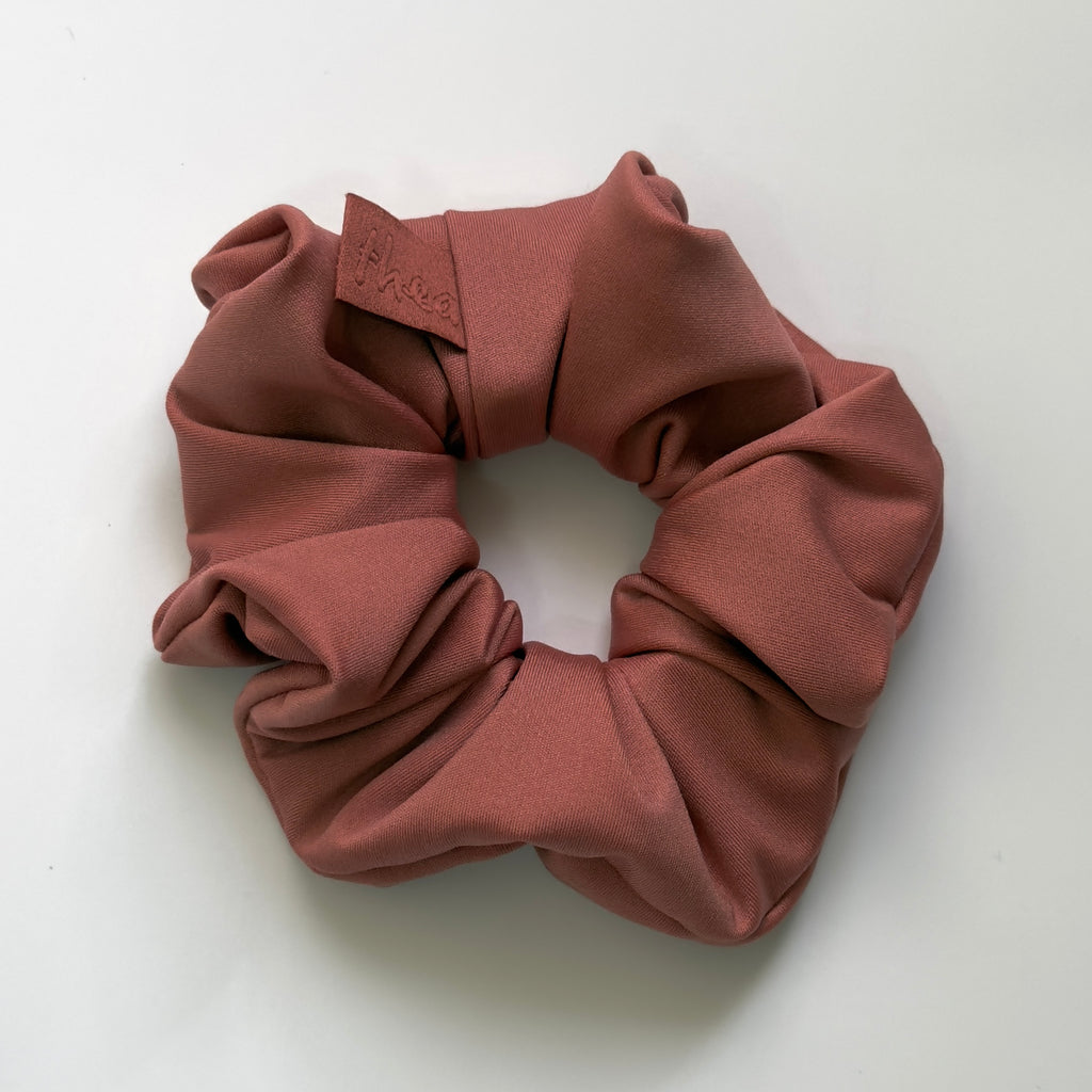 A dusty rose fabric scrunchie with a small leather brand tab that reads 'Mia Rose', photographed on a clean white background.